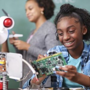 Junior high school age, African American teenage girl works on building a robot in technology class in school classroom setting.  STEM topics.